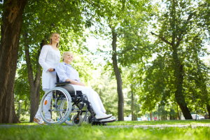 Assistent går med eldre dame i rullestol i en park